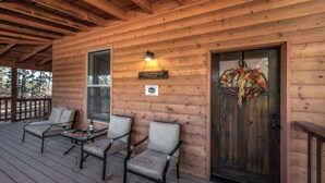 A wooden cabin with a porch, two chairs, a table, a welcome sign, and a door with a wreath. - Sandy Bear - Stunning cabin in the Heart of Ruidoso w priv tub (Ruidoso)