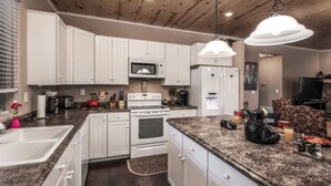 A kitchen with white cabinets, a granite countertop, a stove, a microwave, and a refrigerator. - Sandy Bear - Stunning cabin in the Heart of Ruidoso w priv tub (Ruidoso)