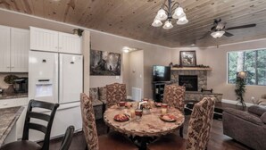 A dining area with a round table, patterned chairs, a white refrigerator, and a stone fireplace. - Sandy Bear - Stunning cabin in the Heart of Ruidoso w priv tub (Ruidoso)