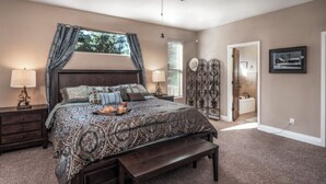 A bedroom with a large bed, bedside tables, a bench, a decorative metal screen, and a framed picture on the wall. - Sandy Bear - Stunning cabin in the Heart of Ruidoso w priv tub (Ruidoso)