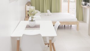 A modern, well-lit room with a bed, a dining table with chairs, a small potted plant, and a TV on a stand. - Prima at Primavera City (Cagayan de Oro)
