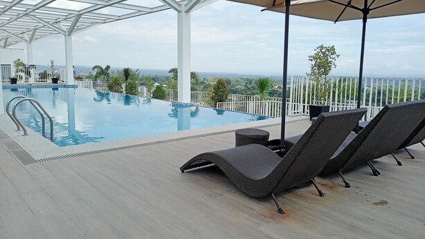 An infinity pool with a white railing, lounge chairs, and a view of the landscape. - Prima at Primavera City (Cagayan de Oro)