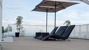 A deck with two lounge chairs and a large umbrella, surrounded by a white fence and potted plants. - Prima at Primavera City (Cagayan de Oro)