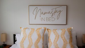Un lit bien fait, avec deux oreillers à motifs chevrons, une table de chevet avec une lampe, et un cadre décoratif au-dessus du lit sur lequel on peut lire : « Restez au lit et méditez. »