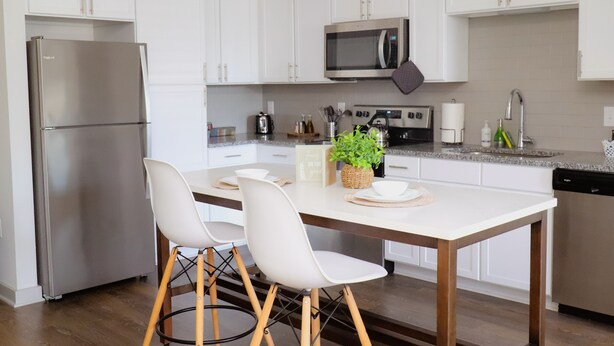 Une cuisine moderne avec des meubles blancs, des appareils en acier inoxydable et une table à manger en bois, assortie de chaises blanches.