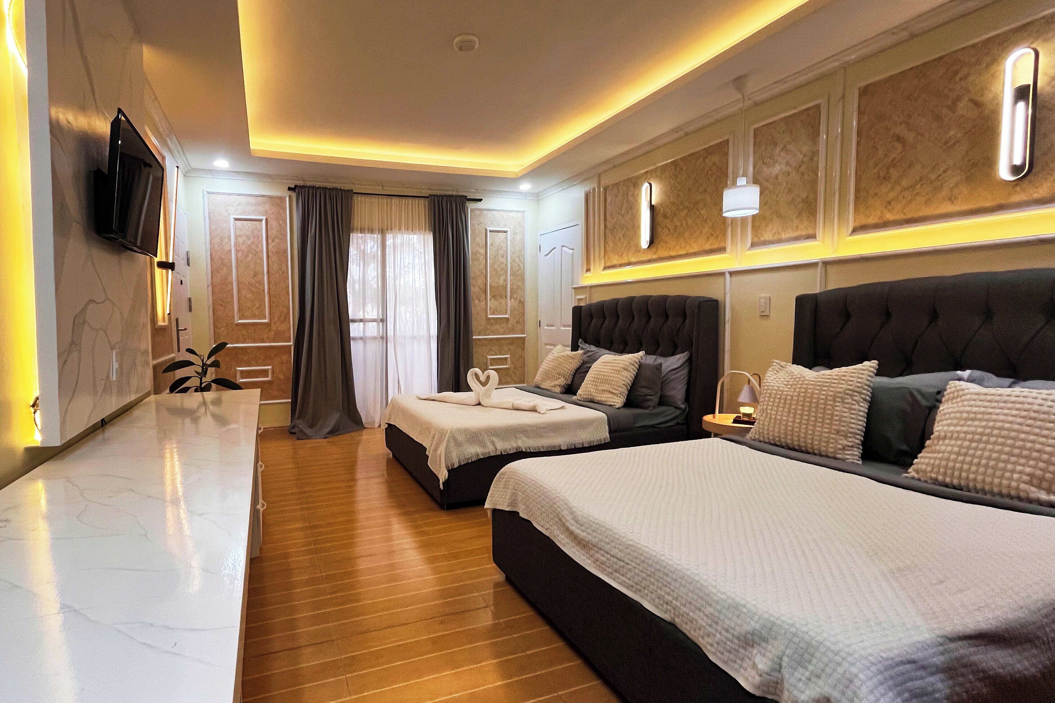 Habitación de hotel con dos camas, televisión, mesita de noche y diseño moderno con suelo de madera e iluminación empotrada.