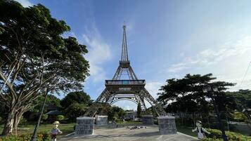 A model of the Eiffel Tower in a park with stone pillars, trees, and a statue of a man.