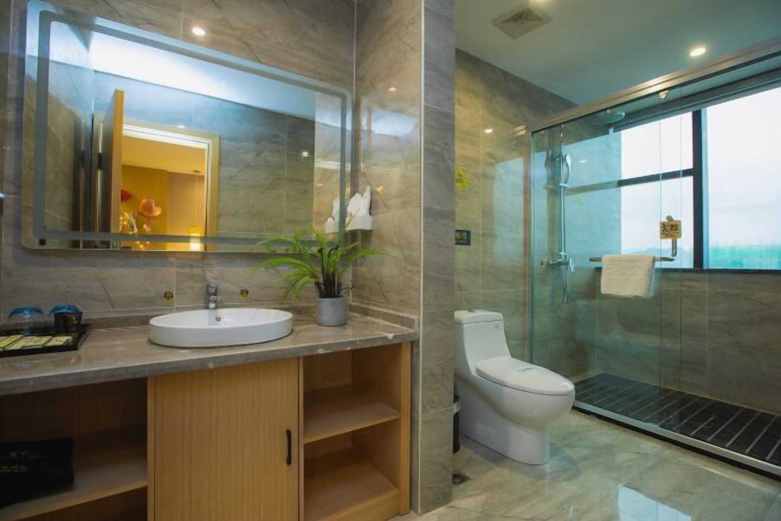 Un baño moderno con un espejo grande, un lavamanos, un inodoro y una ducha con mampara de vidrio.