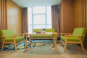 A room with a wooden paneled wall, a green sofa, two green chairs, a wooden table, and a large window with curtains.