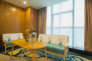 Habitación de hotel con pared de madera, un sofá con motivos de renos, una mesa redonda de madera y un ventanal con cortinas.