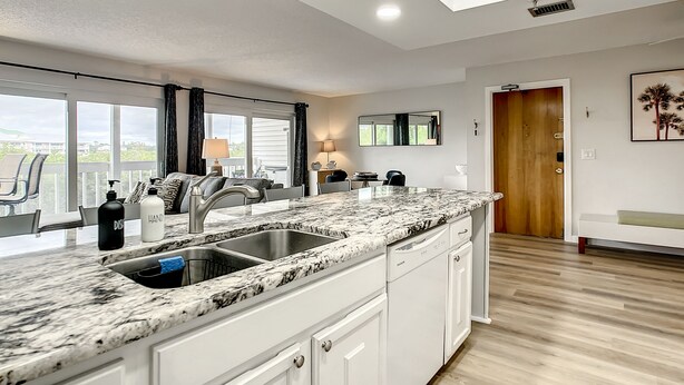 A modern kitchen with a large island, white cabinetry, and a view of the outdoors. - ★Gulf Coast 107★ Heated Pool + Beach Gear, Steps to Beach! Clean&Spacious Condo (Indian Shores)