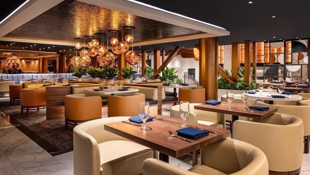 Un restaurant moderne avec de hauts plafonds, un éclairage chaleureux et différents types de sièges, notamment des tables et des banquettes.