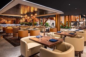 Un restaurant moderne avec de hauts plafonds, un éclairage chaleureux et différents types de sièges, notamment des tables et des banquettes.