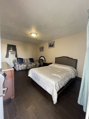 A hotel room with a bed, a desk, a chair, and a small table. - Rancho Motel (Ontario)