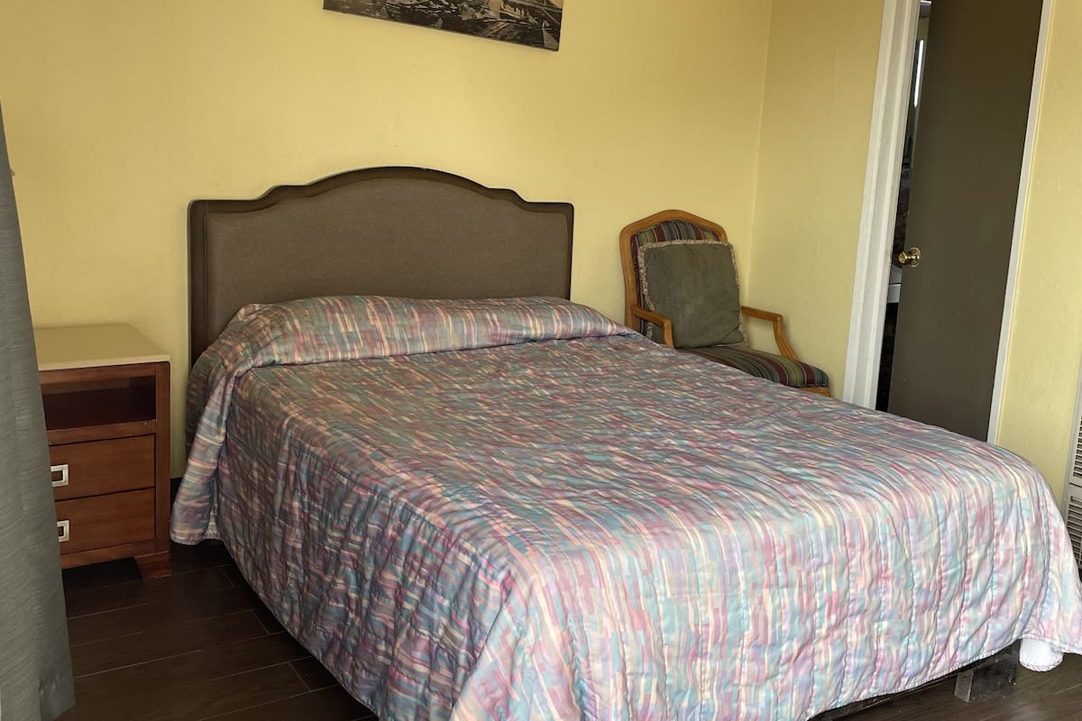 A bedroom with a bed, a nightstand, a chair, a door, and a painting on the wall.