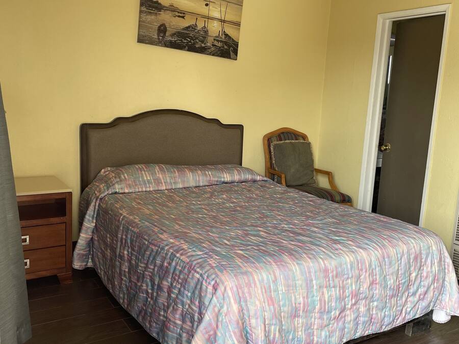 A bedroom with a bed, a nightstand, a chair, a door, and a painting on the wall.