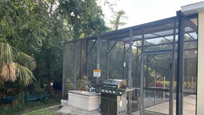 Ein überdachter Grillbereich mit Glasfassade, eine Beton-Sitzbank und ein Warnschild.