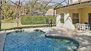 Ein Pool mit gewölbter Kante, umgeben von einer überdachten Terrasse mit Stühlen und einem Tisch.