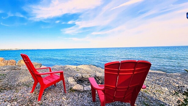 Deux chaises rouges placées sur un rivage rocheux, avec vue sur l’océan.