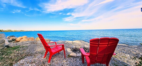 Two red chairs by a rocky shore with a view of the ocean.