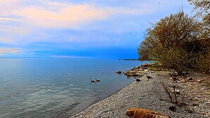Un lac paisible, avec une rive de galets et une jetée qui s’étend au loin.
