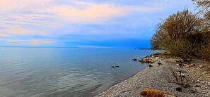 A calm lake with a pebbled shore and a distant pier.