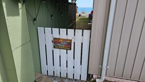 A white wooden gate with a sign that reads "Welcome to our Cabin. It's always 5 o'clock here. Please bring your own water. Relax, refresh, renew."