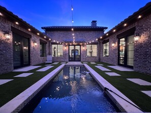 A modern house with a swimming pool, stone walls, and outdoor lighting.