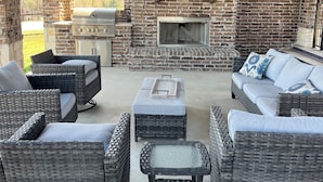 Une terrasse extérieure aménagée avec des meubles en osier, une cheminée en pierre et un barbecue.