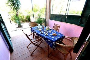 Un patio con una mesa lista para comer, sillas de mimbre y una planta en maceta.