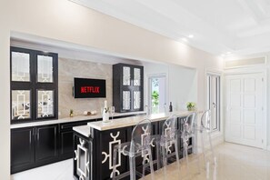 Een moderne keuken met een bar, een wandtelevisie en transparante stoelen.