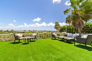 An outdoor seating area with multiple chairs and tables, surrounded by a white balustrade, under a clear sky. - Aruba Beach Retreat by Bocobay (Noord)