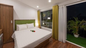 A hotel room with a bed, a green headboard, a nightstand, a window with curtains, and a potted plant. - AMI Old Quarter Hotel (Hanoi)