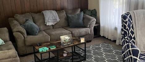 A living room with a brown sofa, a patterned rug, a coffee table, and a chair with a blue and white design.