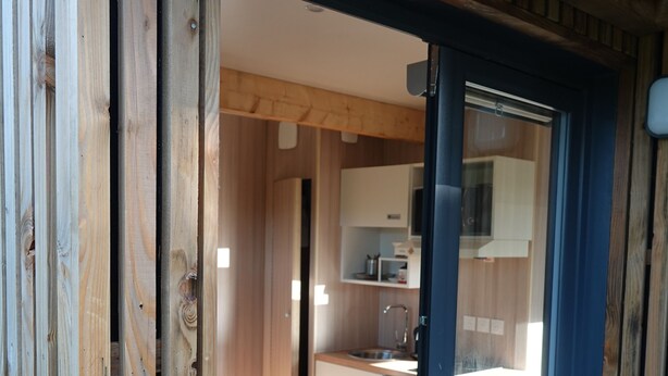 Puerta de madera que da a una cocina moderna con armarios blancos y un microondas integrado.