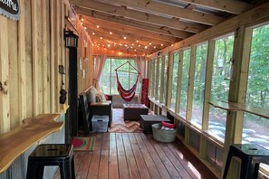 Une terrasse en bois avec un hamac, un coin salon et de grandes fenêtres donnant sur une forêt.