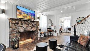 Un salon moderne avec une cheminée en pierre, un téléviseur à écran plat, un canapé en cuir et un escalier.