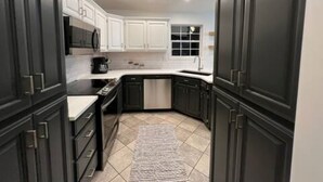 A modern kitchen with dark cabinetry, a white countertop, and a tiled floor.