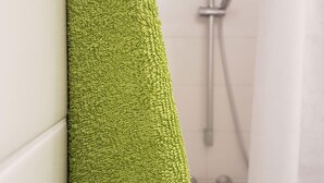 Uma toalha verde pendurada em uma parede num banheiro, com um chuveiro visível ao fundo.