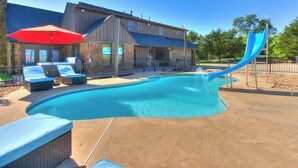 A swimming pool with lounge chairs and a slide, surrounded by a building with a patio. - POOL, HOT TUB, AMAZING TURF, GAMES GALORE LUXURY VILLA IN OKC (Oklahoma City)