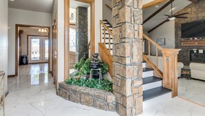 A spacious living area with a stone fireplace, a wooden staircase, and a large mirror. - POOL, HOT TUB, AMAZING TURF, GAMES GALORE LUXURY VILLA IN OKC (Oklahoma City)