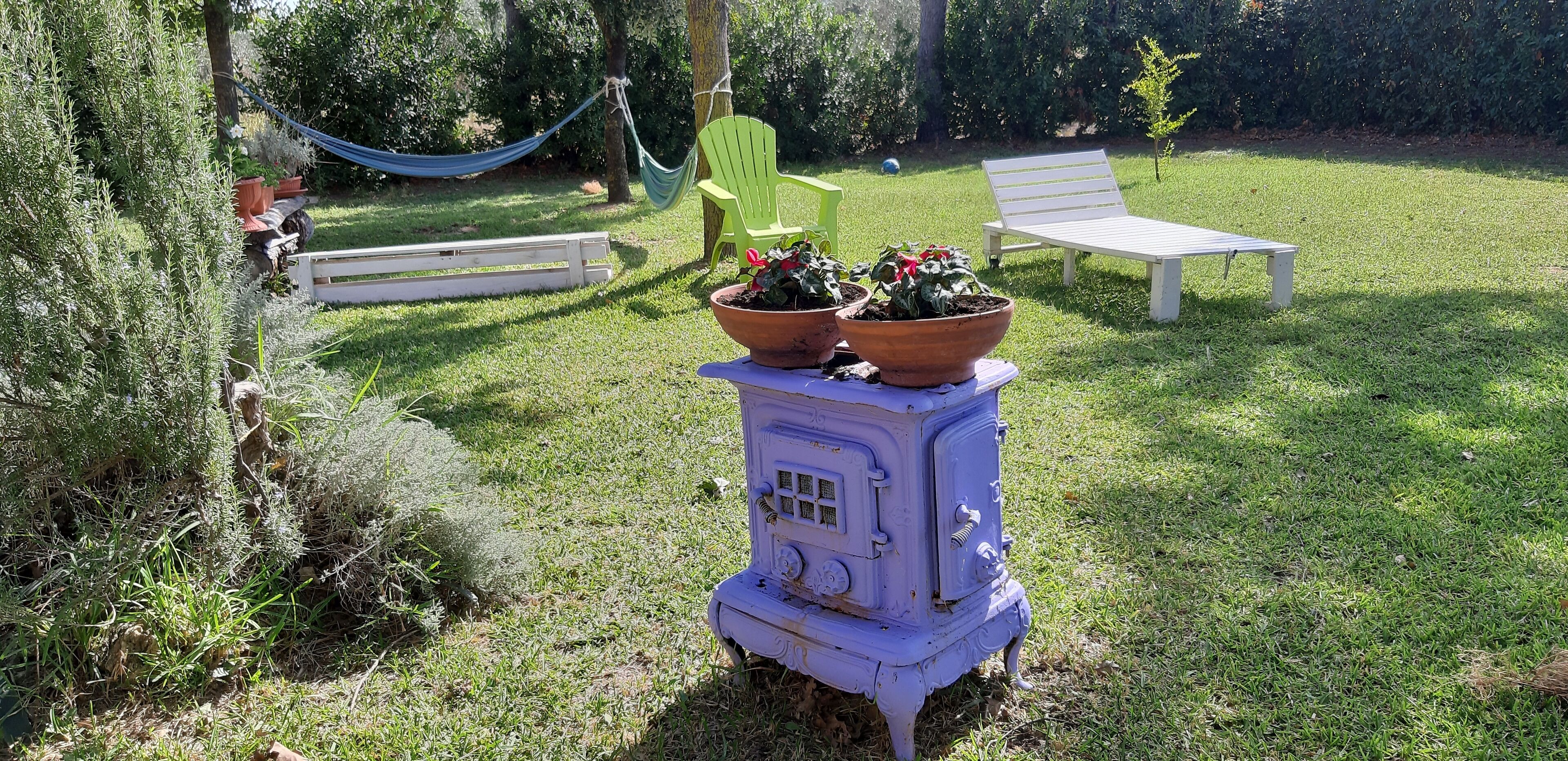 Un espace extérieur aménagé avec un vieux poêle, des chaises vertes et un hamac.
