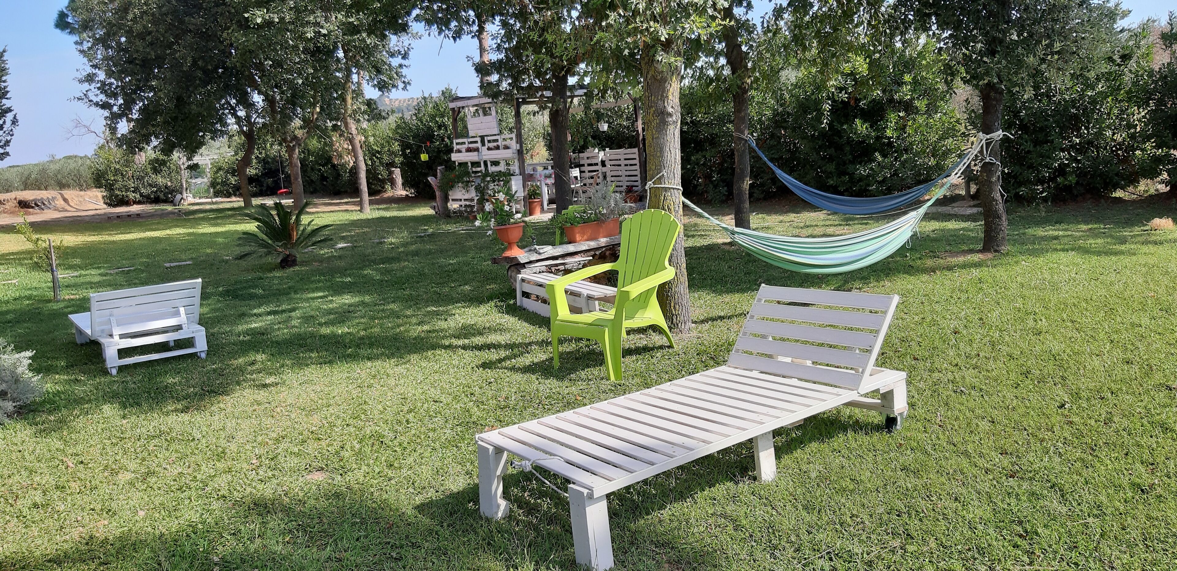 A grassy outdoor area with two white benches, a green chair, and a hammock.