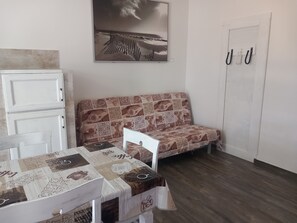 Ein Zimmer mit Holzboden, einem weißen Sofa mit gemustertem Bezug, einem weißen Tisch mit Kaffeebruch-Tischdecke, einem weißen Schrank und einer Tür mit Haken.