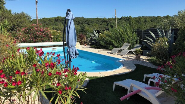 Une piscine entourée de chaises longues et protégée par un parasol.