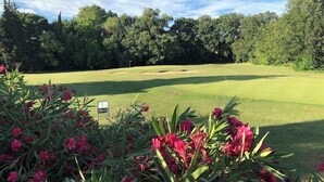 Un parcours de golf sous un ciel dégagé, entouré d’une forêt dense.