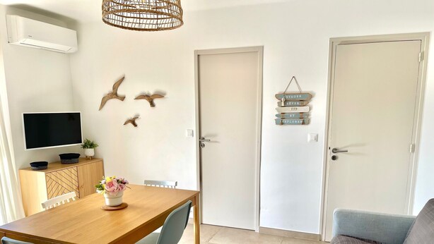 A dining area with a wooden table, two chairs, a TV on a cabinet, and a door with a sign above it.