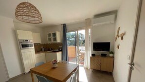 A compact kitchen with a built-in oven, a dining table with two chairs, and a TV on a wooden cabinet.