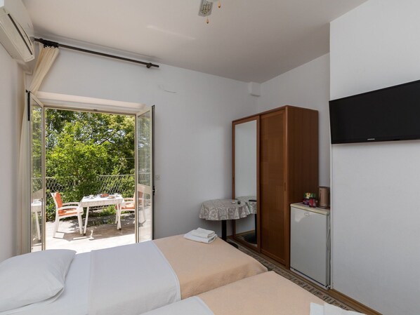 A bedroom with two beds, a wardrobe, a TV, and a balcony with a table and chairs.