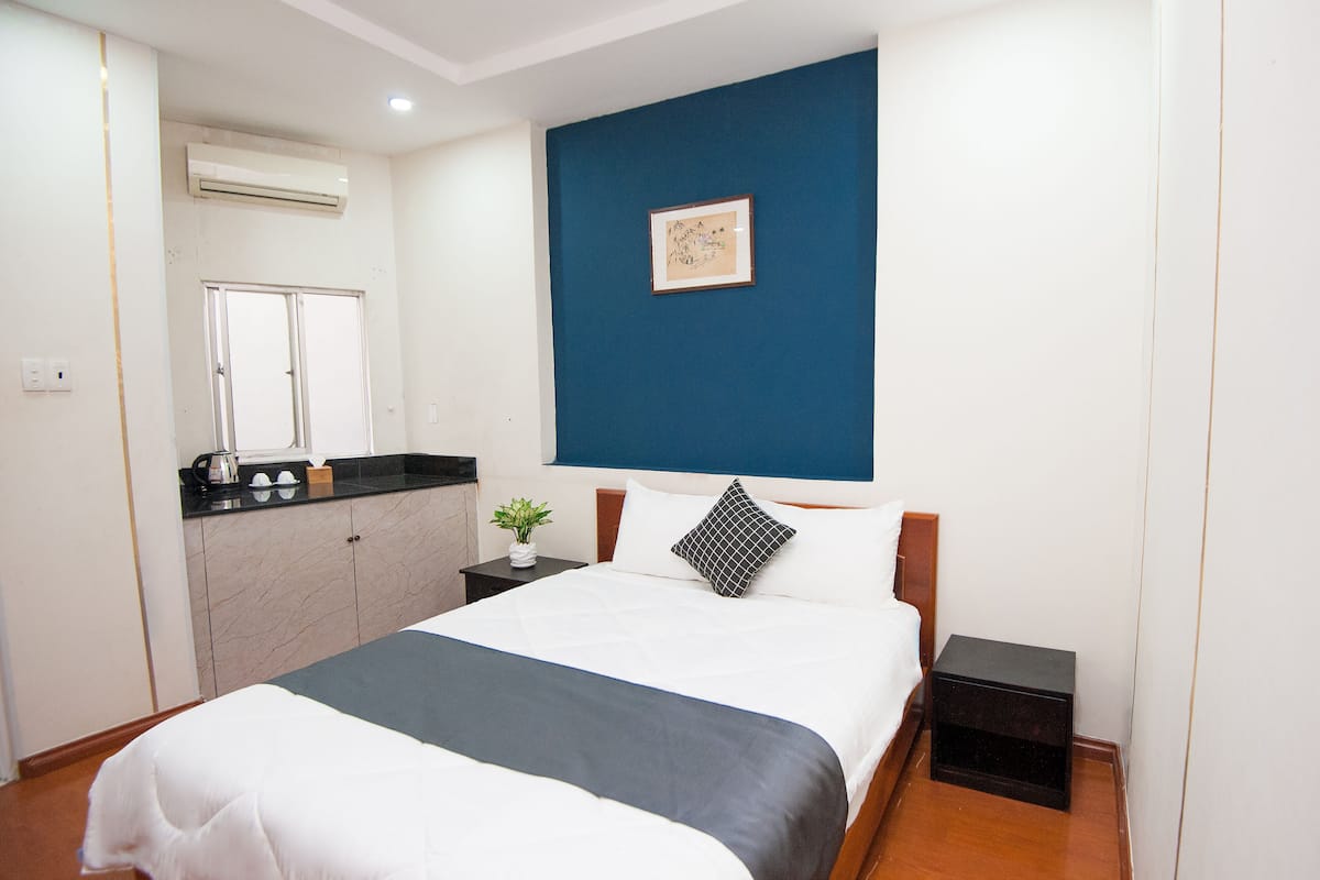 A neatly arranged hotel room with a bed, bedside tables, a small plant, and a wall-mounted air conditioner.